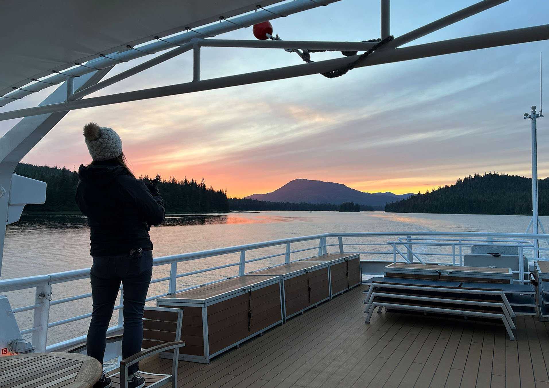 a woman standing on the deck of the ship, watching a sunrise